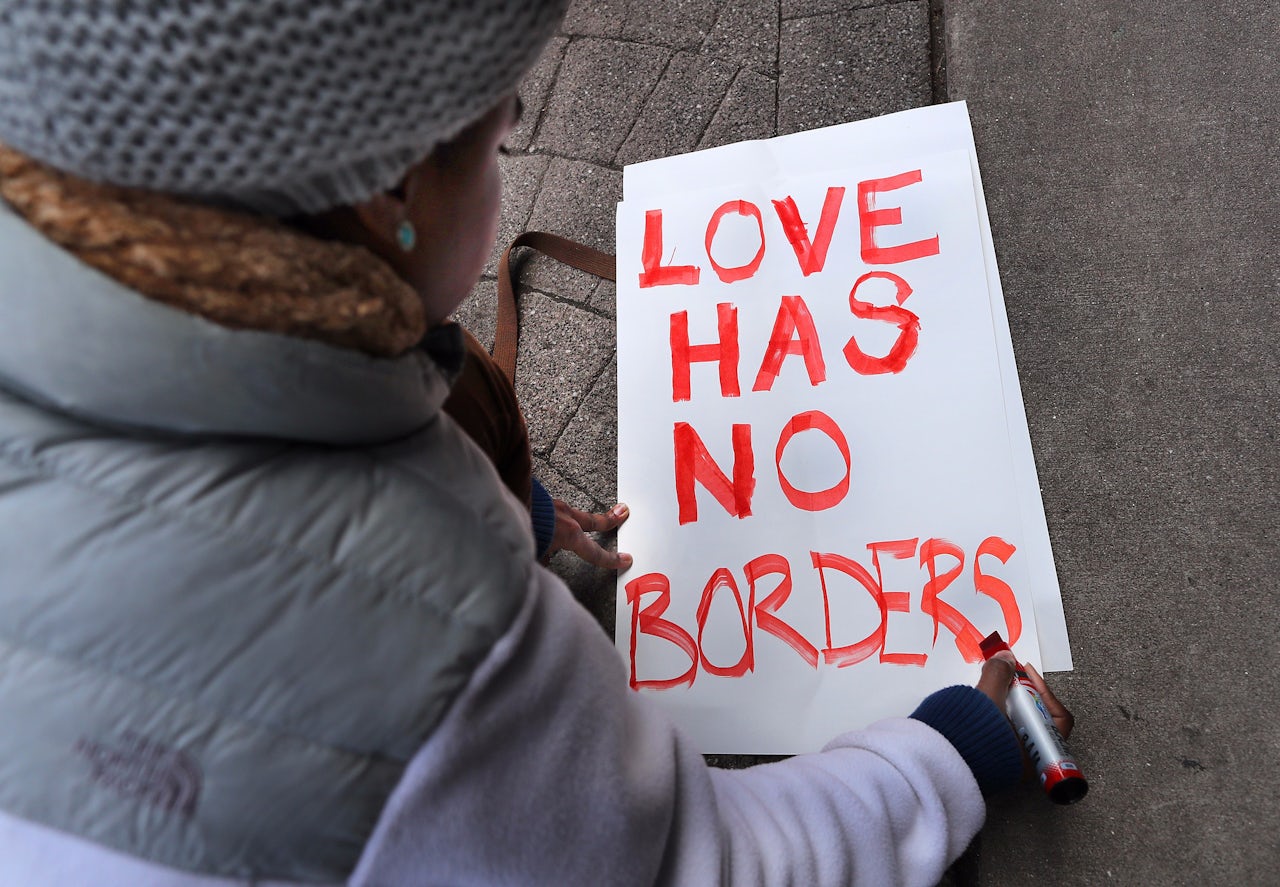 Tori Furtado, from Boston, kneels down to write a sign that reads, 'Love has no borders.'