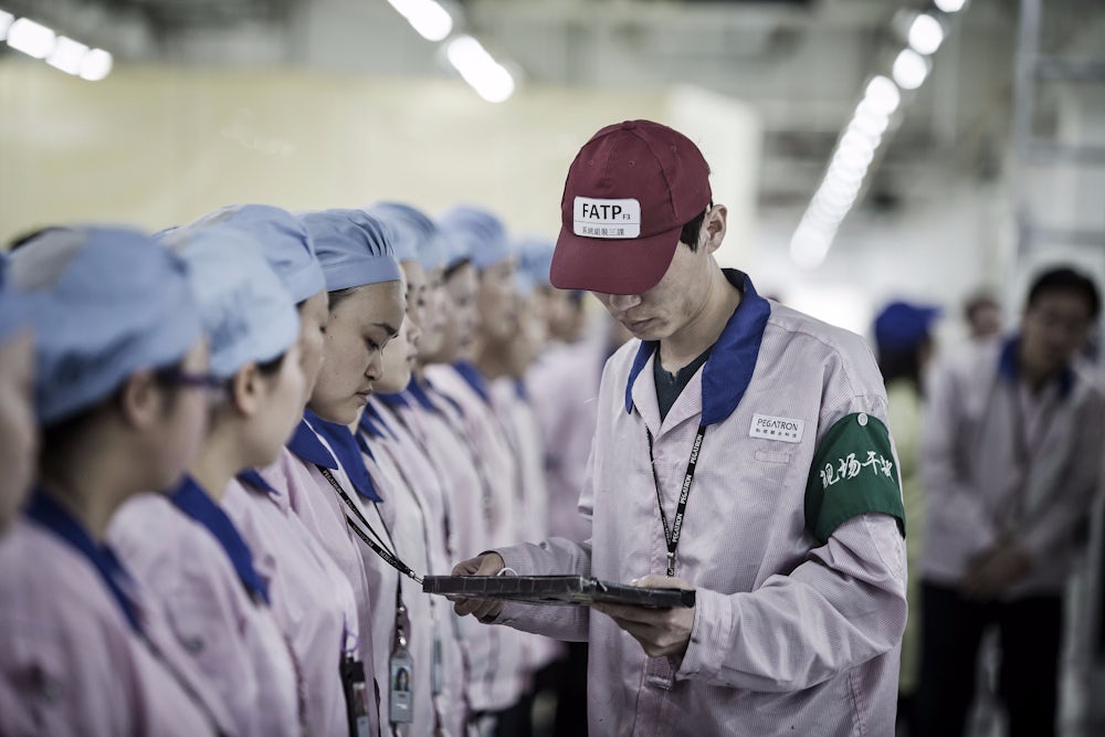 A supervisor holding an Apple Inc. iPad checks an employee's badge during roll call at a Pegatron Corp. factory in Shanghai, China.