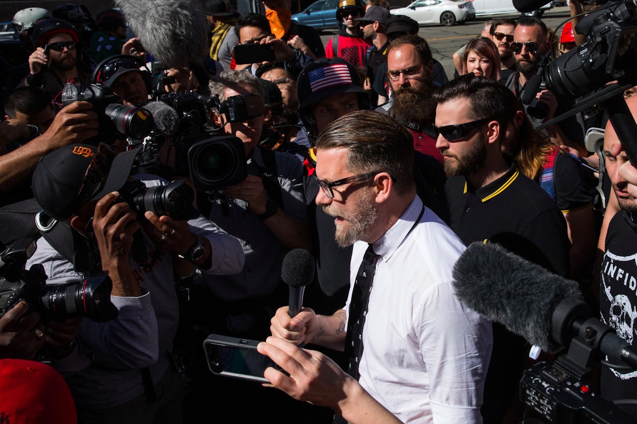 A member of the Proud Boys stands behind Gavin McInnes in a black and yellow Fred Perry polo, at a rally in Berkeley, California.