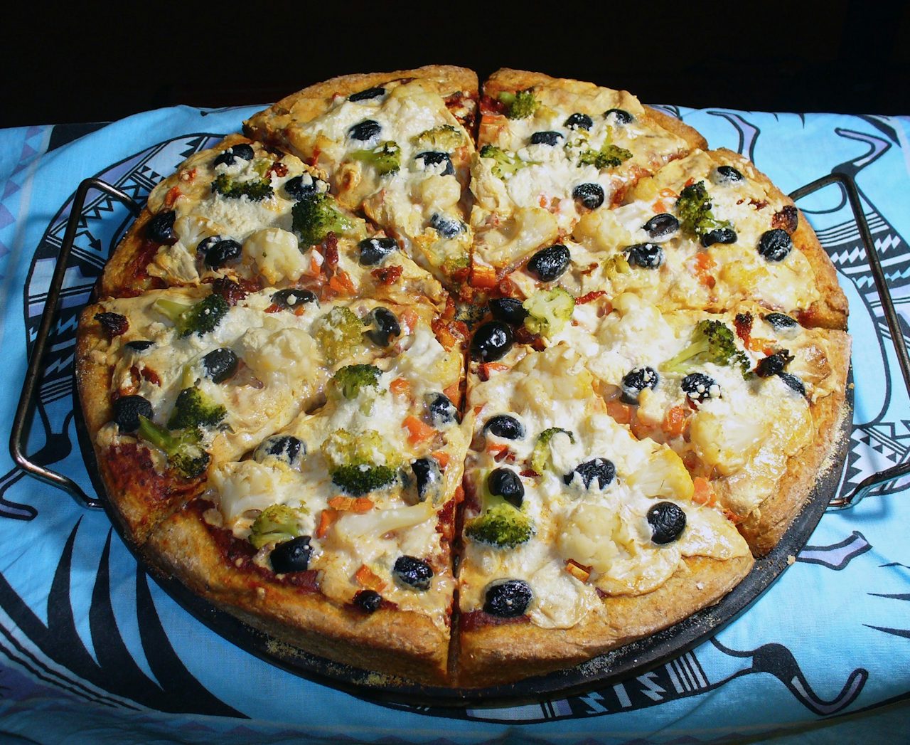 A homemade veggie lover's pizza with broccoli, cauliflower, carrots, sundried tomatoes, black olives, red sauce, and mozzarella Daiya cheese.