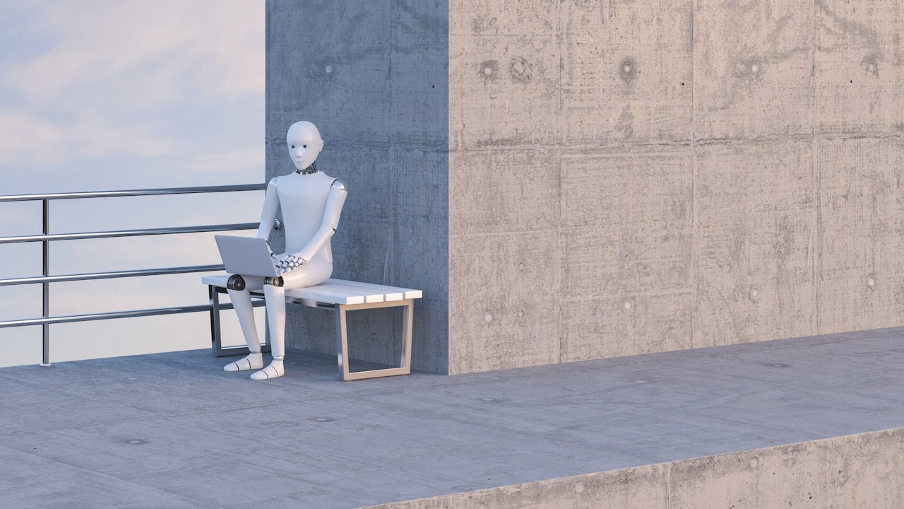 Robot sitting on bench, using laptop.