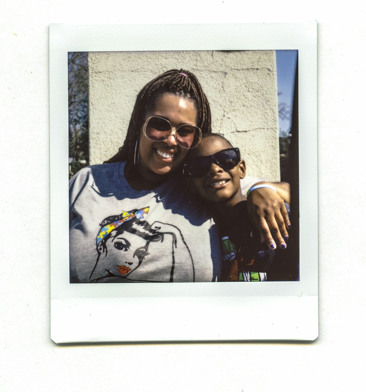 A woman and a young boy smile in a photo together. The woman wears a bandana with the multicolored jigsaw pattern that represents autism awareness.