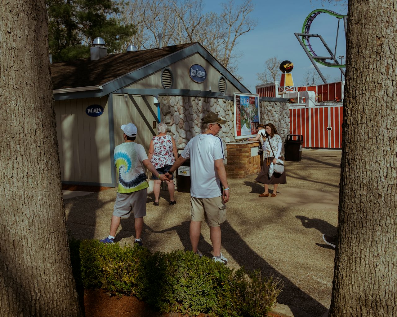 A man and a young boy hold hands outside of a restroom adjacent to the Bizarro roller coaster.