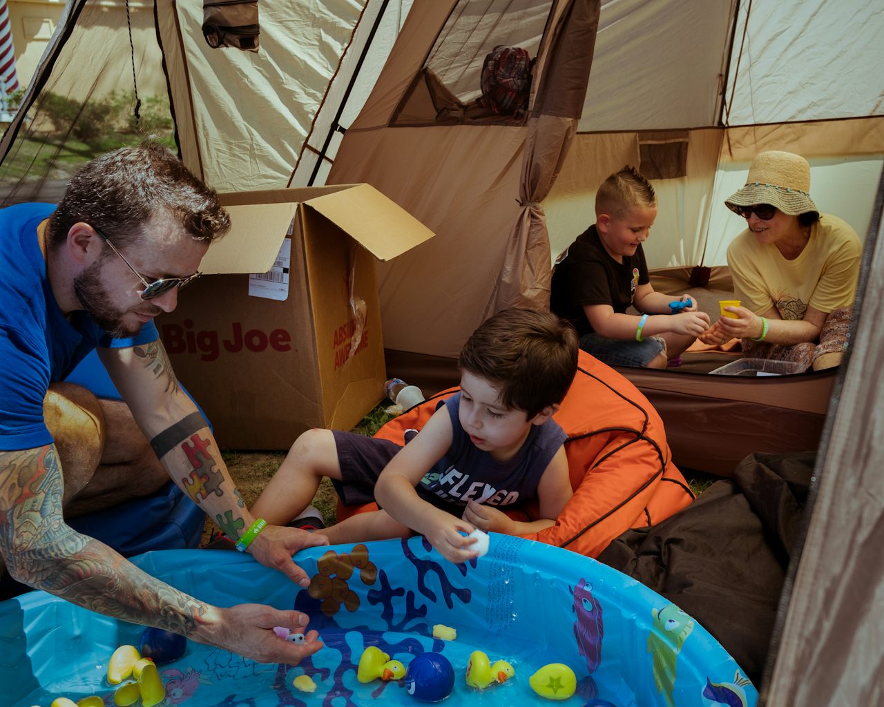 In a waterside Decompression Tent by the Six Flags Fantasy Forest, a man shares a moment with a young boy. The multicolored puzzle tattoo pattern on his forearm represents autism awareness.